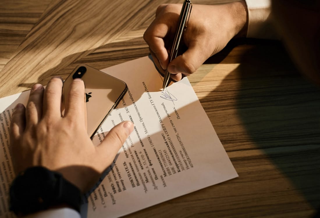 A hand signing a legal document at a wooden desk